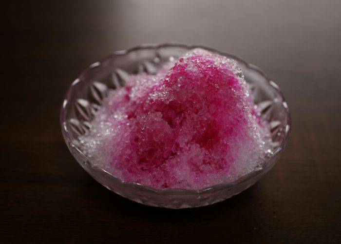 Japanese shaved ice with pink syrup in an etched glass dish.